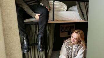 A bunk bed room with a wooden bunk bed, a lower bunk with a mattress and pillows, and a curtain.