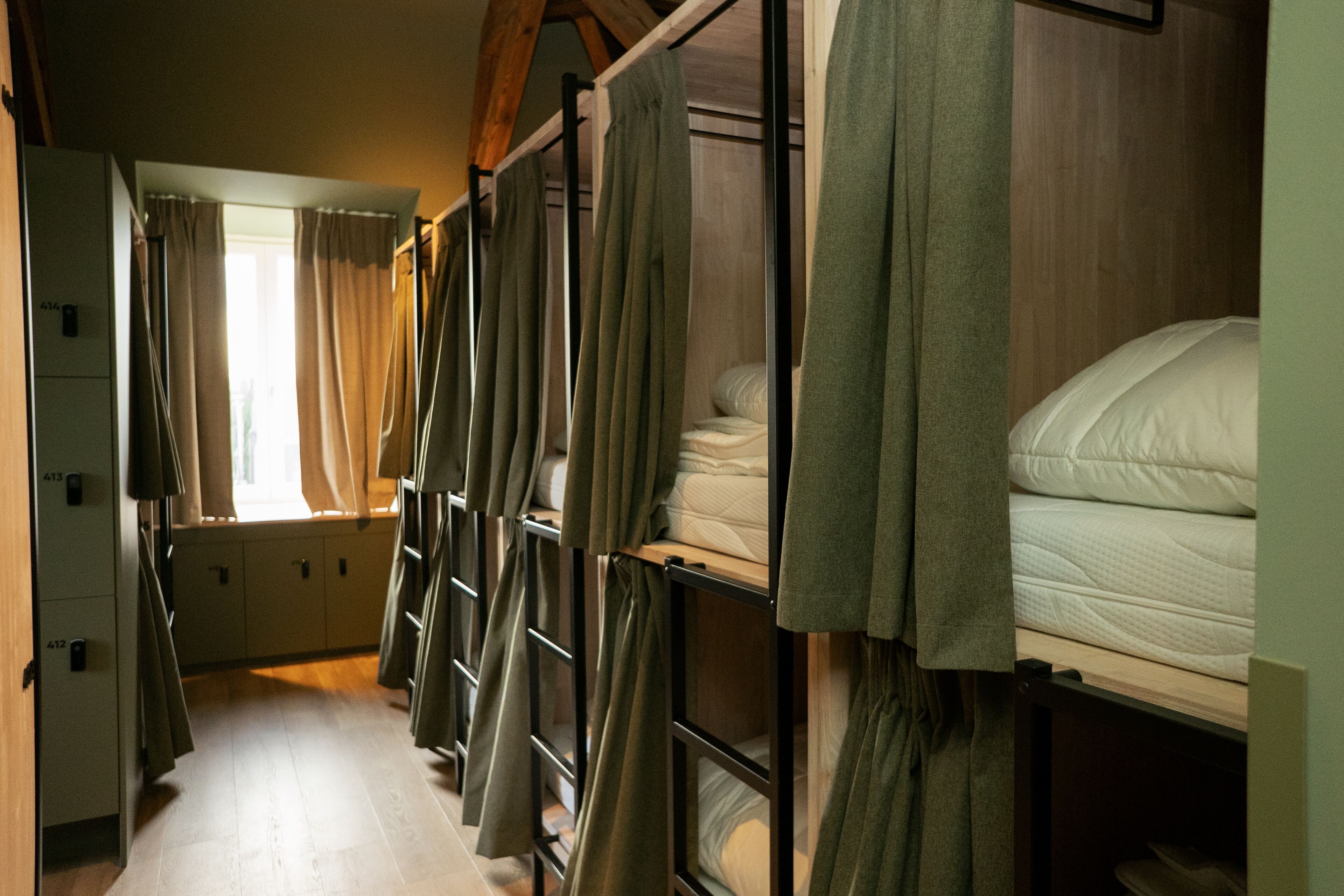 A corridor with bunk beds, each with a mattress and pillows, and curtains.