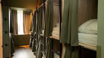 A corridor with bunk beds, each with a mattress and pillows, and curtains.