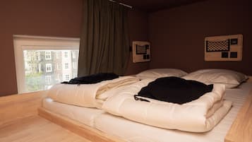 A bedroom with a bed, a window with curtains, and a view of buildings outside.
