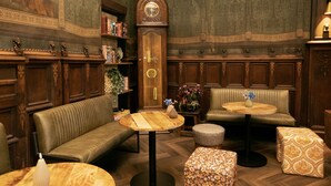 Un interno classico con una panca di legno, un tavolo rotondo, una sveglia e una libreria.
