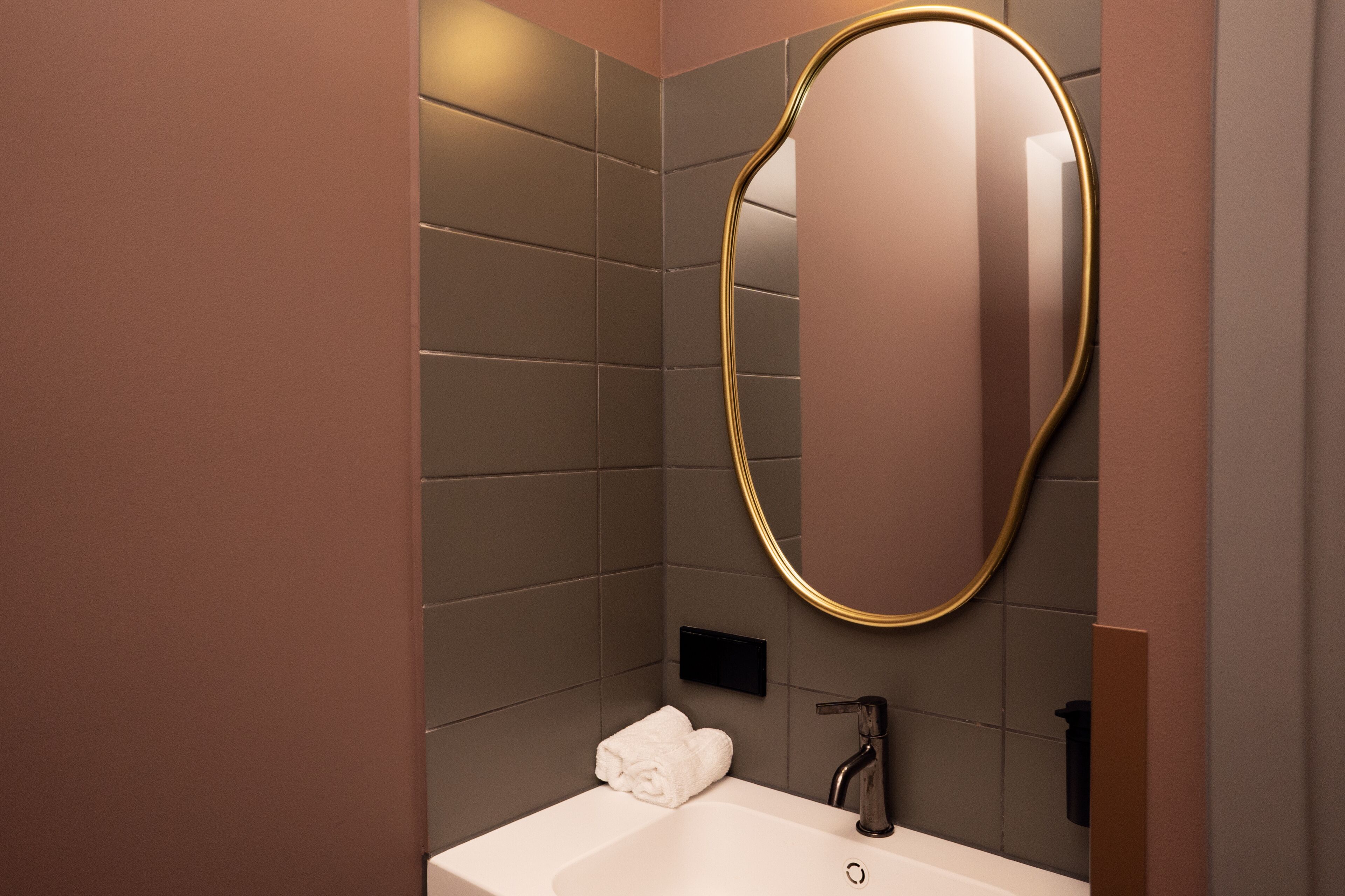 Un baño moderno con un lavamanos blanco, un espejo con marco dorado y una toalla sobre el mostrador.