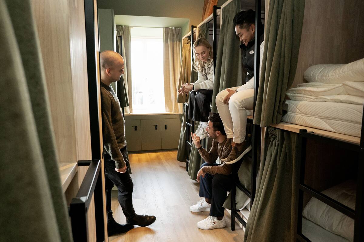 A dormitory room with bunk beds, a window with curtains, and a wooden floor.