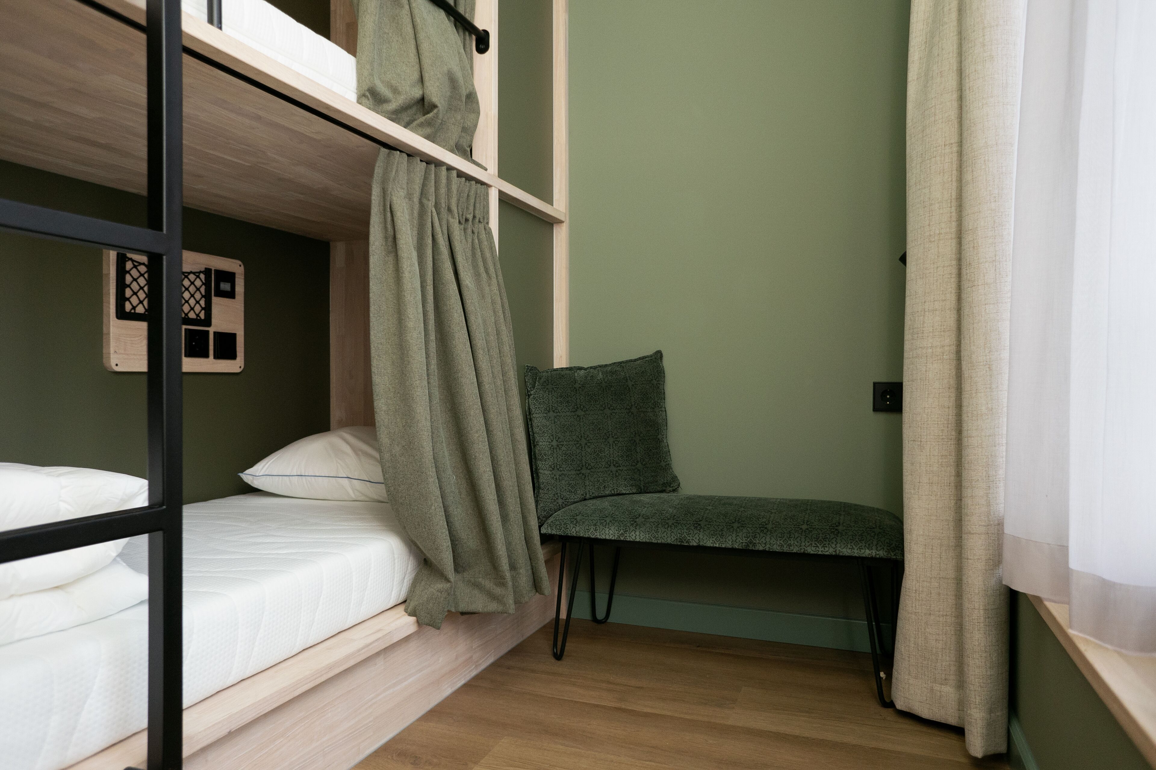 Un lit superposé avec une couverture verte, une chaise et un plancher en bois.