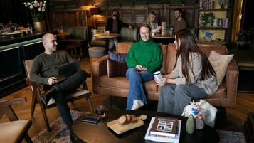 A cozy lounge area with leather sofas, a coffee table with snacks, and a bookshelf in the background.