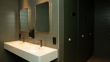 Een moderne badkamer met een wit wastafelmeubel, twee spiegels en een donkere deur.