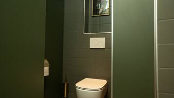 A bathroom with a toilet, a hand dryer, and a framed picture on the wall.