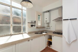 A kitchen with a window, double sink, stove, and white cabinets. - Charming Apartment in the Castle (Lisbon)