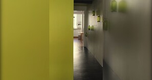 Un pasillo de diseño moderno, con suelo oscuro y paredes claras. Hay luces verdes fijadas a la pared y se ve un área de cocina al fondo.