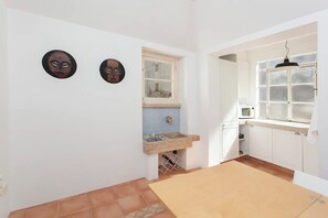 A kitchen with white cabinets, a window, a sink with a marble countertop, and two wall-mounted decorative masks.