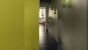 Un pasillo de diseño moderno, con suelo oscuro y paredes claras. Hay luces verdes fijadas a la pared y se ve un área de cocina al fondo.
