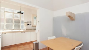 Cocina compacta con armarios blancos, una mesa de madera y un ventanal con vidrio esmerilado.