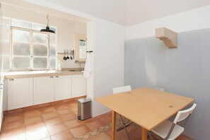 Une cuisine de taille réduite, avec des meubles blancs, une table en bois et une fenêtre à vitrage dépoli.