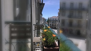 Una calle estrecha flanqueada por edificios, con un balcón que tiene una maceta, y un cielo despejado.