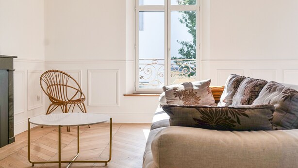 Un salon avec un canapé blanc, une table ronde et un fauteuil en osier.