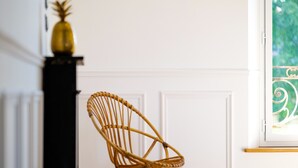 Une chaise en osier dans une pièce aux murs recouverts de panneaux blancs et dotée d’une fenêtre ornée de vitraux.