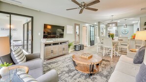 A spacious living room with a ceiling fan, a dining area with a table and chairs, and a kitchen in the background.