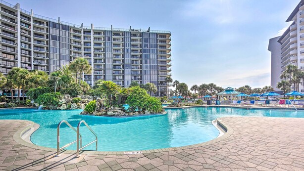 A hotel with a large swimming pool surrounded by palm trees and a landscaped area.