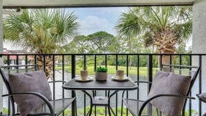 A balcony with a table and chairs, overlooking a body of water and palm trees.