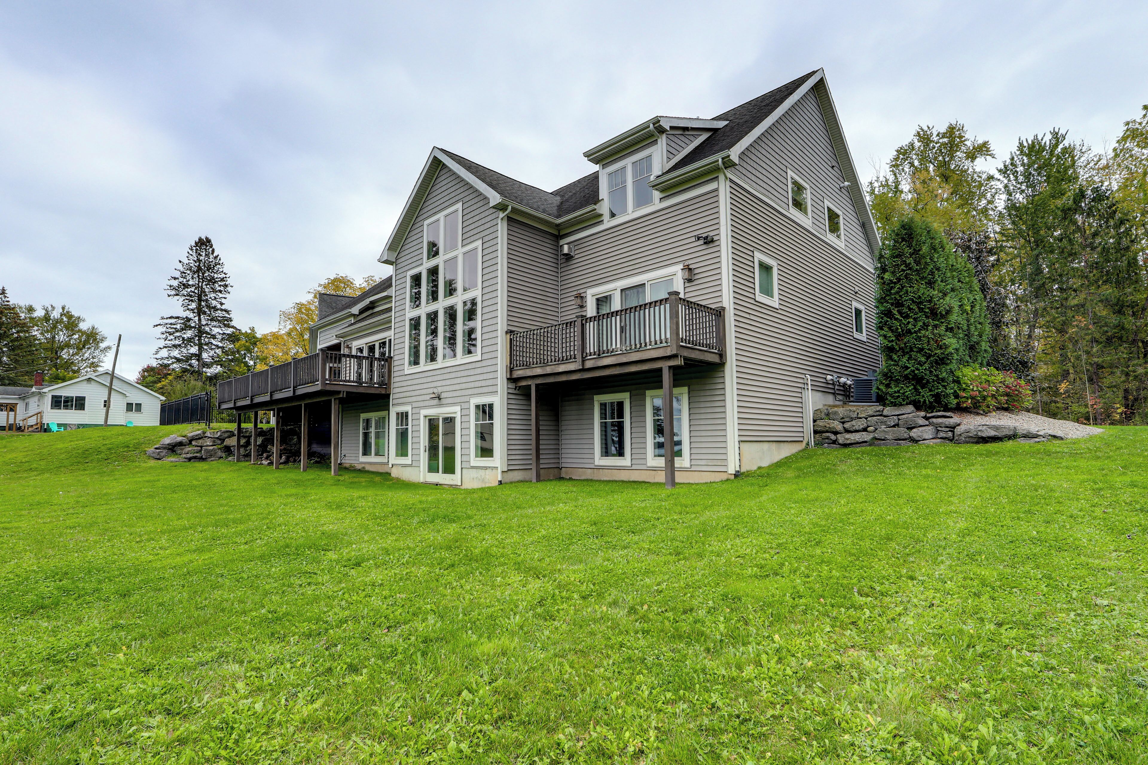 A two-story house with a large front lawn, a covered porch, and a stone retaining wall.