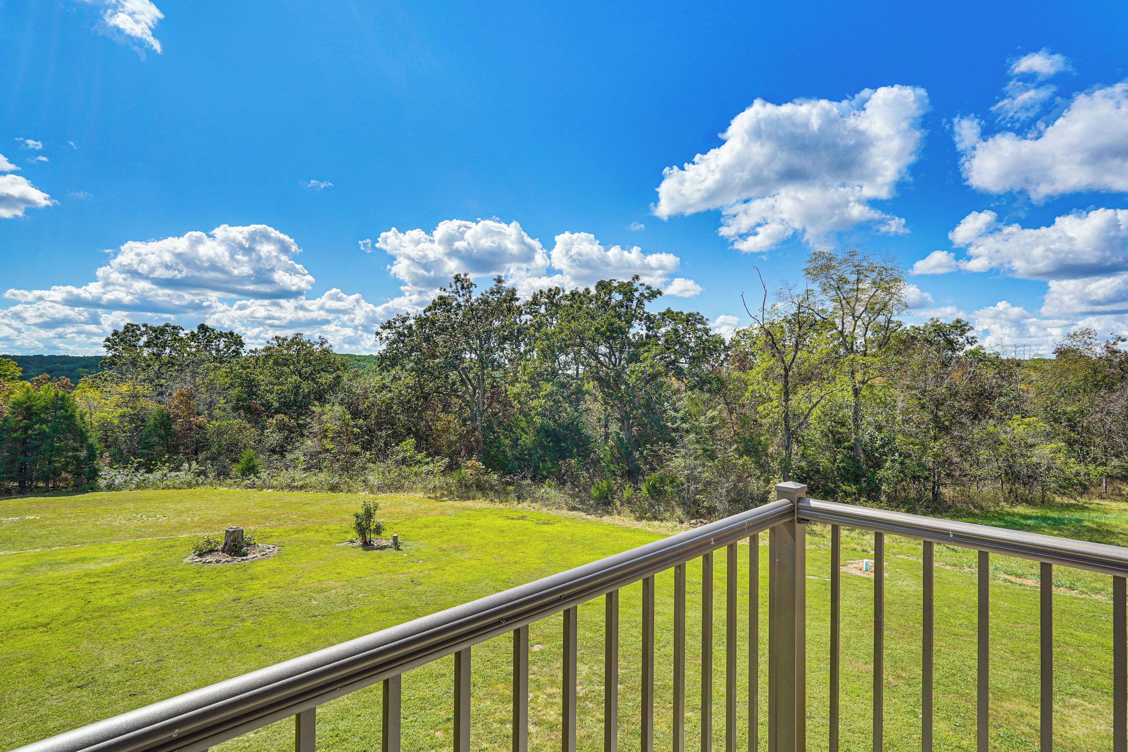 A balcony with a metal railing overlooking a grassy lawn with trees and a clear blue sky.
