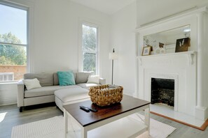 A living room with a sofa, a coffee table, a fireplace, and a large window. - Walk to Churchill Downs: Pet-friendly Retreat! (Louisville)