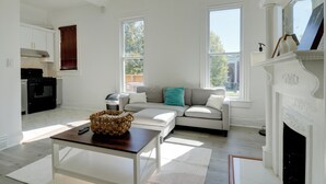 A modern living room with a sofa, a fireplace, and a kitchen area. - Walk to Churchill Downs: Pet-friendly Retreat! (Louisville)