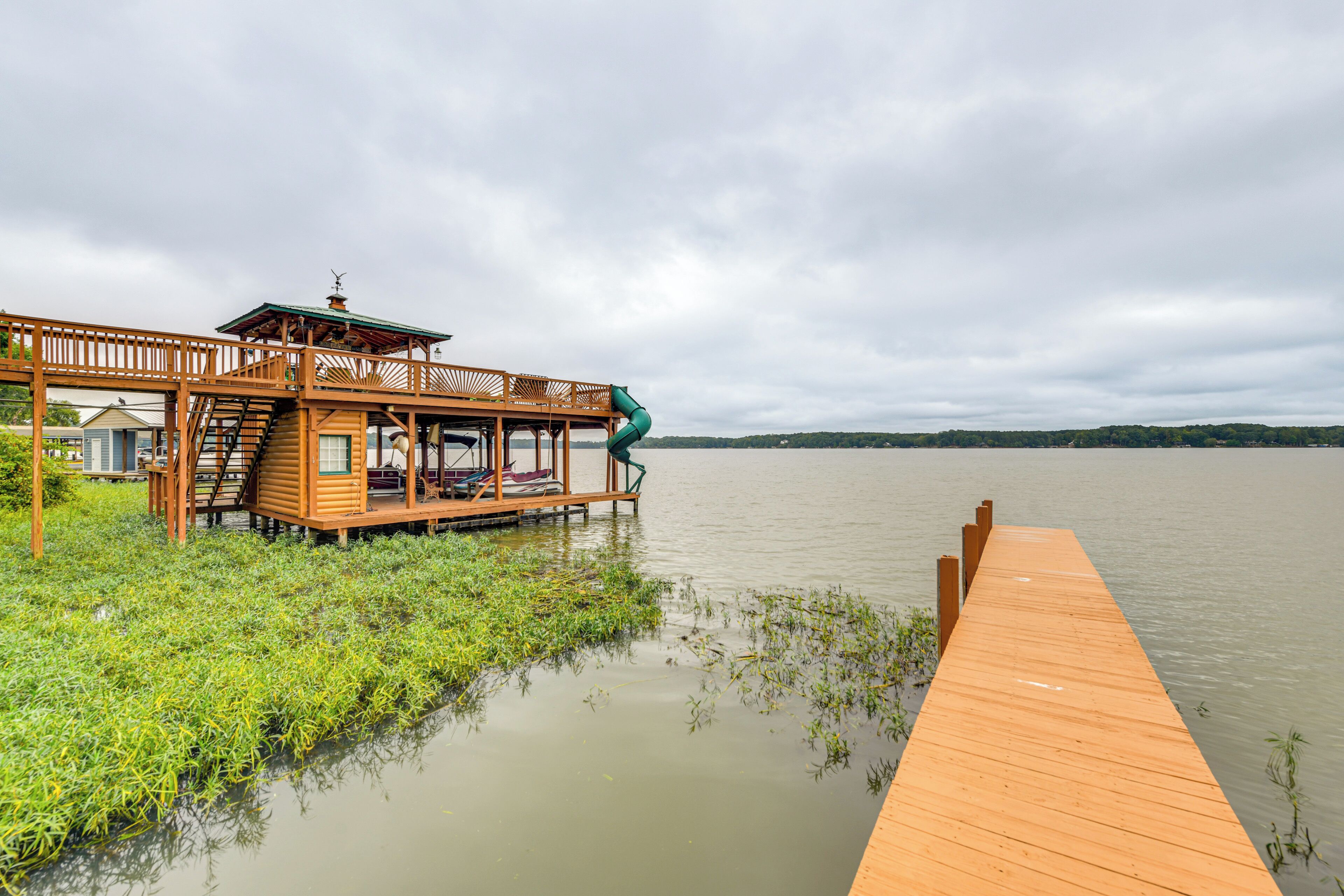 Une jetée en bois s’étendant sur un lac paisible, avec une structure en bois comprenant un espace de repos abrité et un escalier menant à une plateforme.