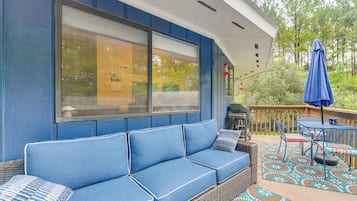 Relax on the outdoor deck with a comfortable sofa and wicker furniture, surrounded by a colorful rug and a scenic view.