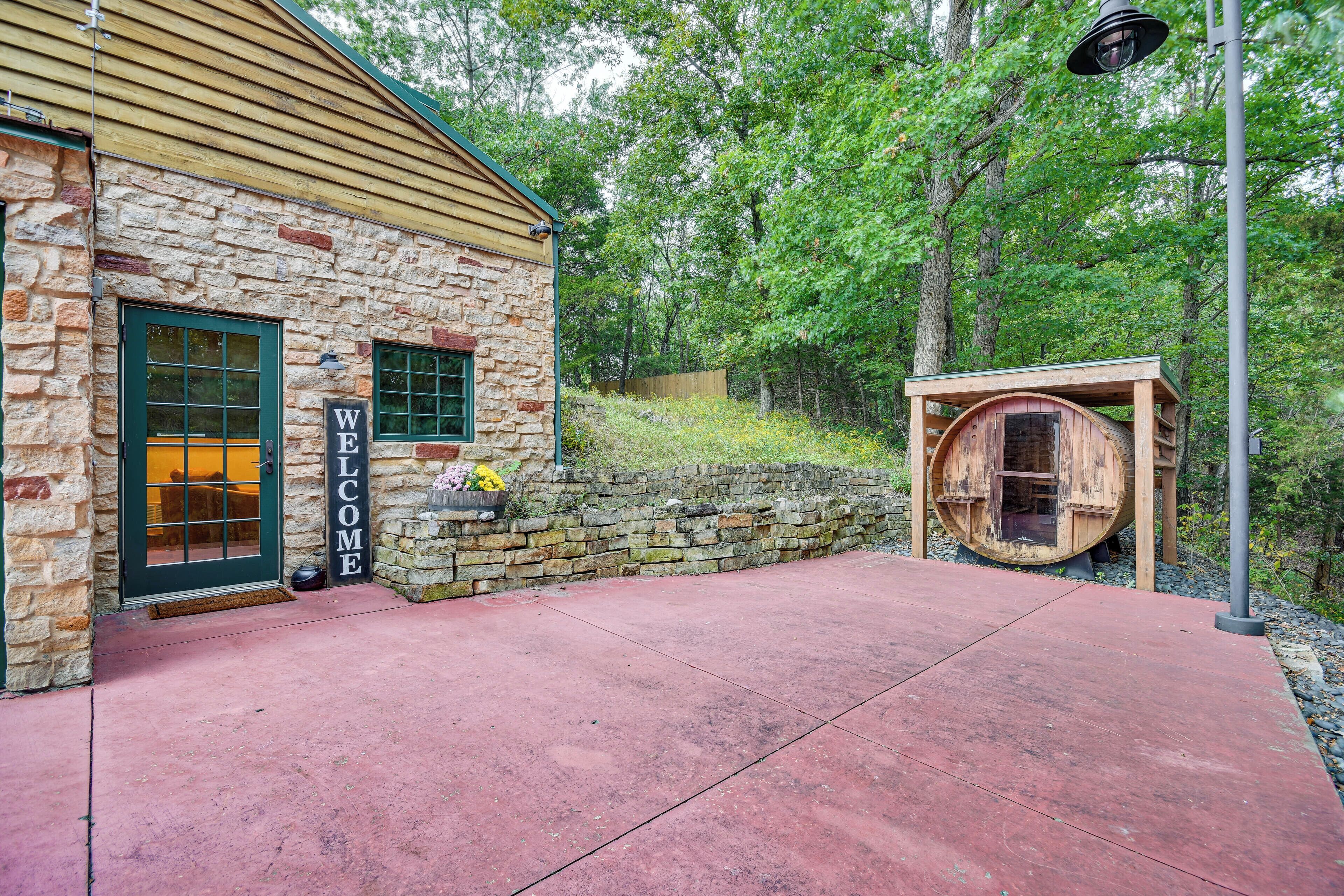A stone building with a 'WELCOME' sign, a wooden barrel structure, and a red concrete patio.