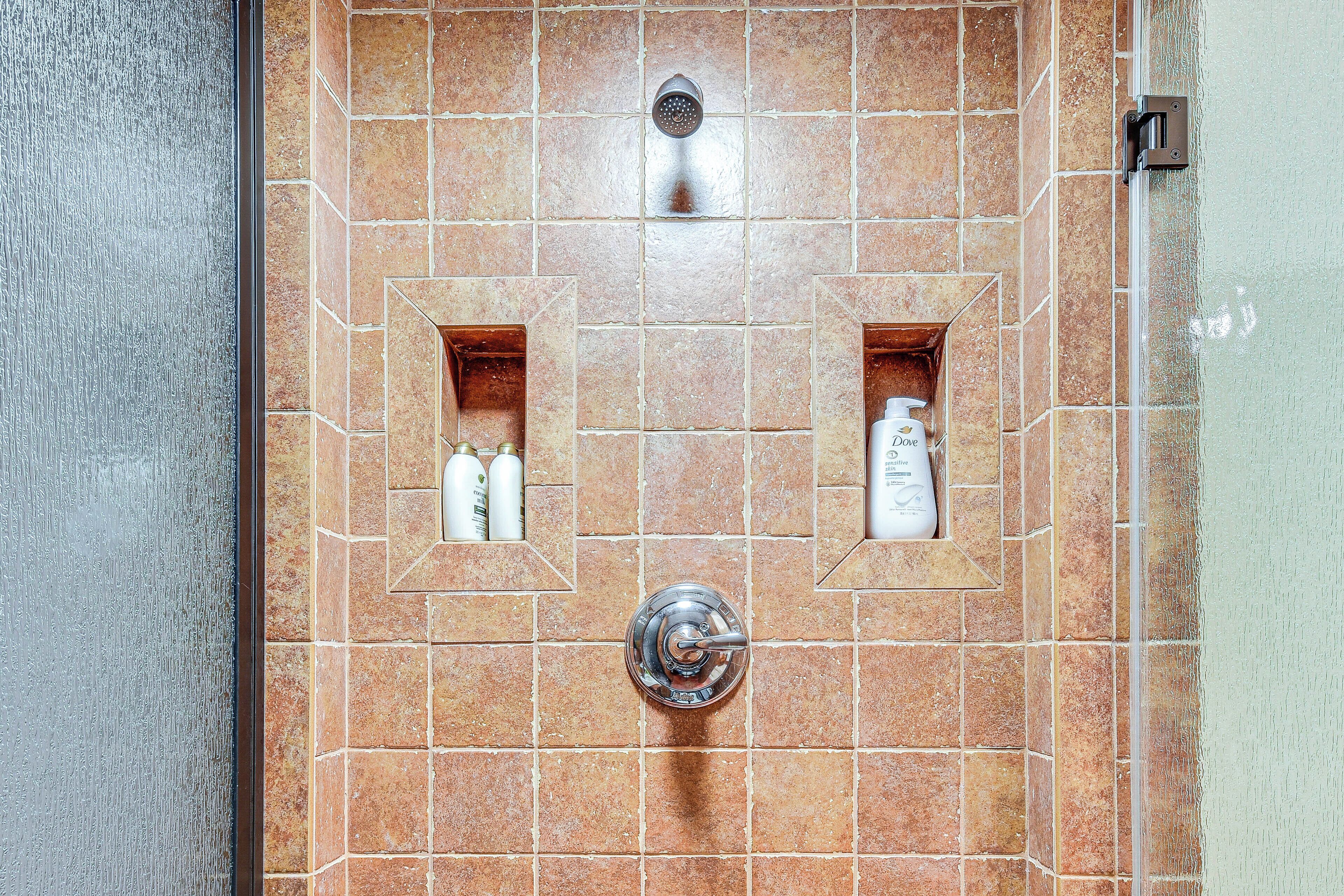 A bathroom with a shower, a towel rack, and two small shelves with toiletries.