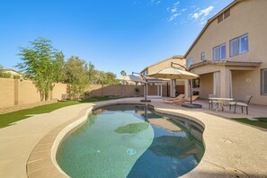 Un patio trasero con piscina, mobiliario de jardín y una zona de estar techada.