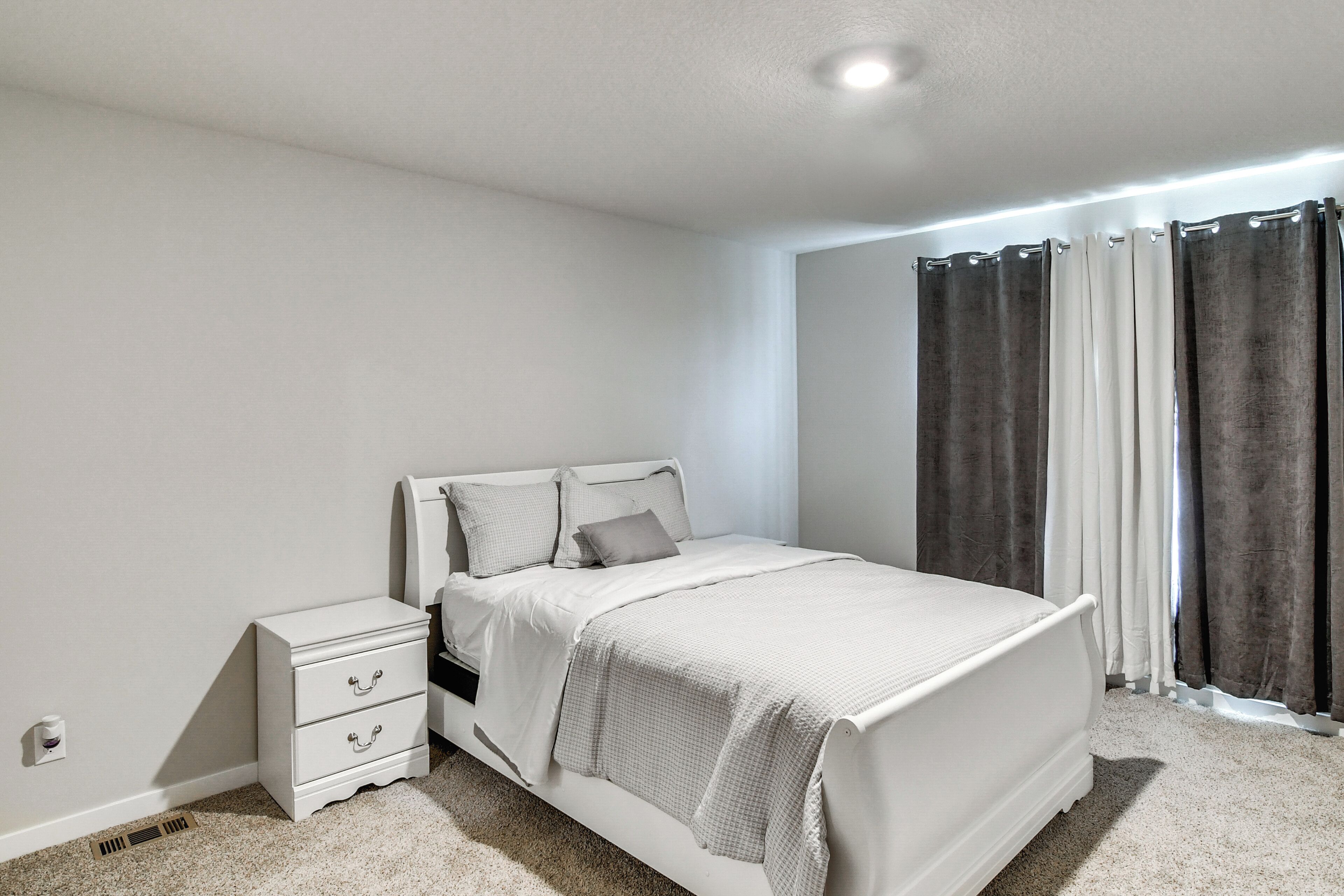 A bedroom with a white bed, a nightstand, and a window with curtains.