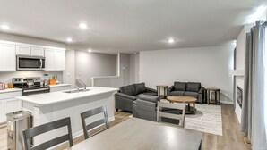 Una cocina moderna con armarios blancos, un microondas y una estufa. Hay un comedor con mesa y sillas, y un sofá gris en la sala.