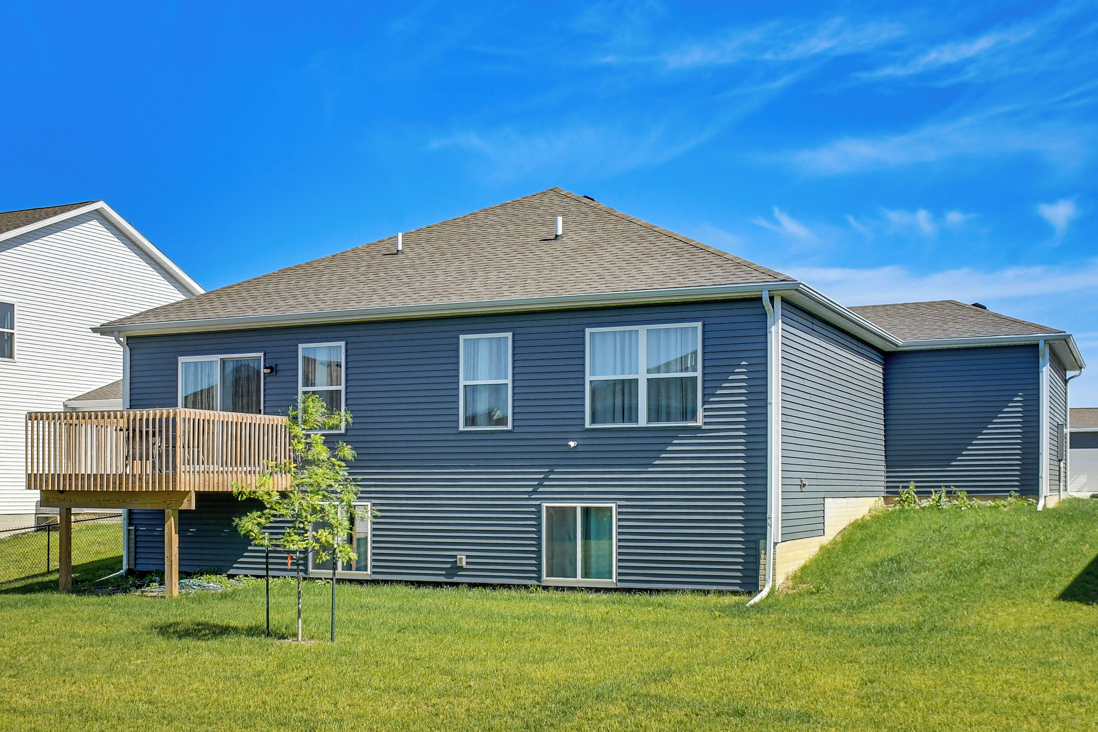 A two-story residential building with a deck, a small tree, and a grassy yard.
