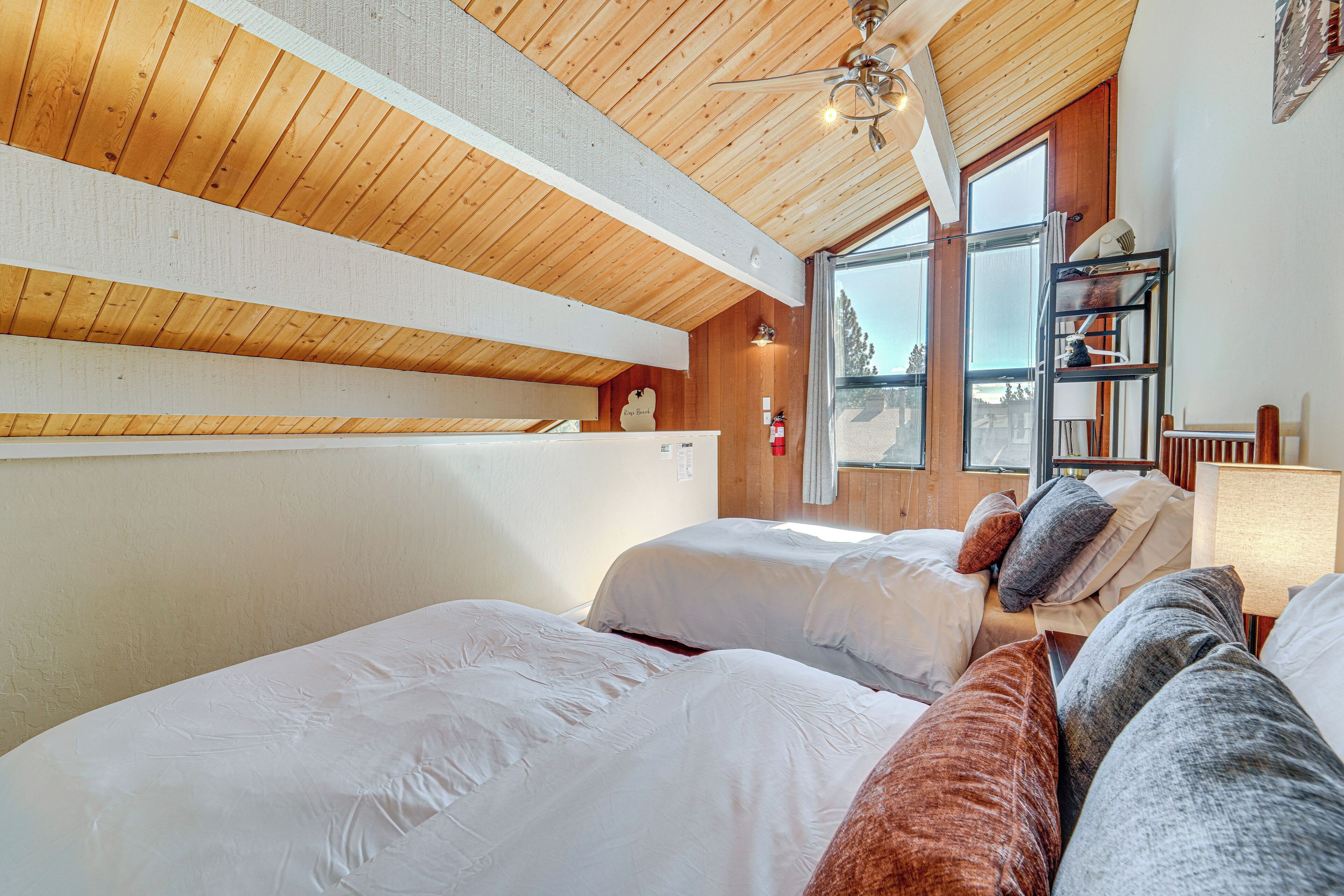 Ein Schlafzimmer mit Holzbalkendecke, zwei Betten mit weißer und brauner Bettwäsche, einem Fenster mit Blick und einem Regal mit Gegenständen.
