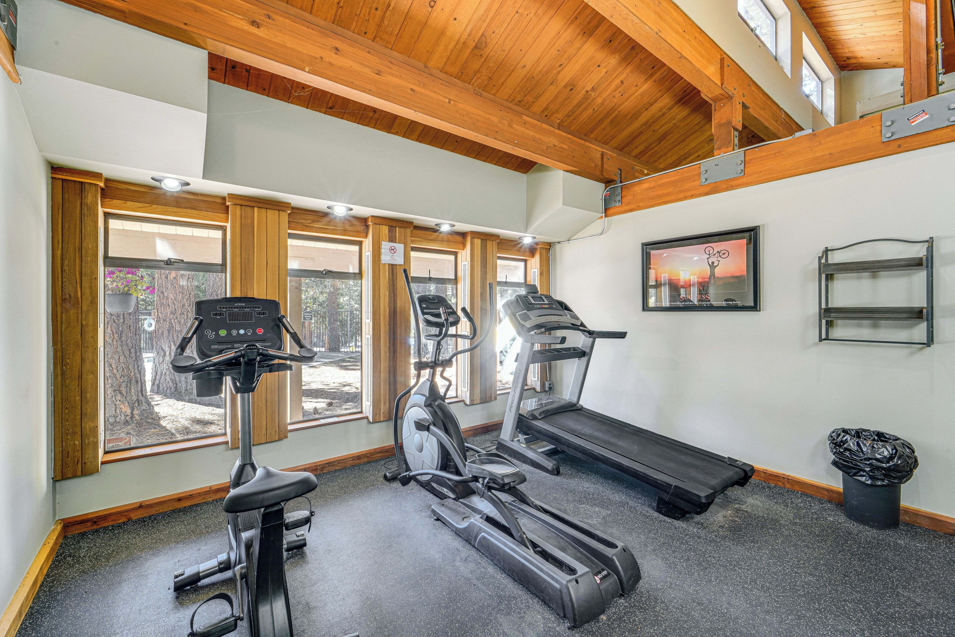 A gym with exercise equipment, large windows, and a wooden ceiling.