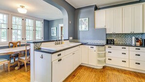 A kitchen with white cabinets, a wooden dining table, and a tiled backsplash. - Near Lake: Historic Boyne City Home w/ Fire Pit! (Boyne City)