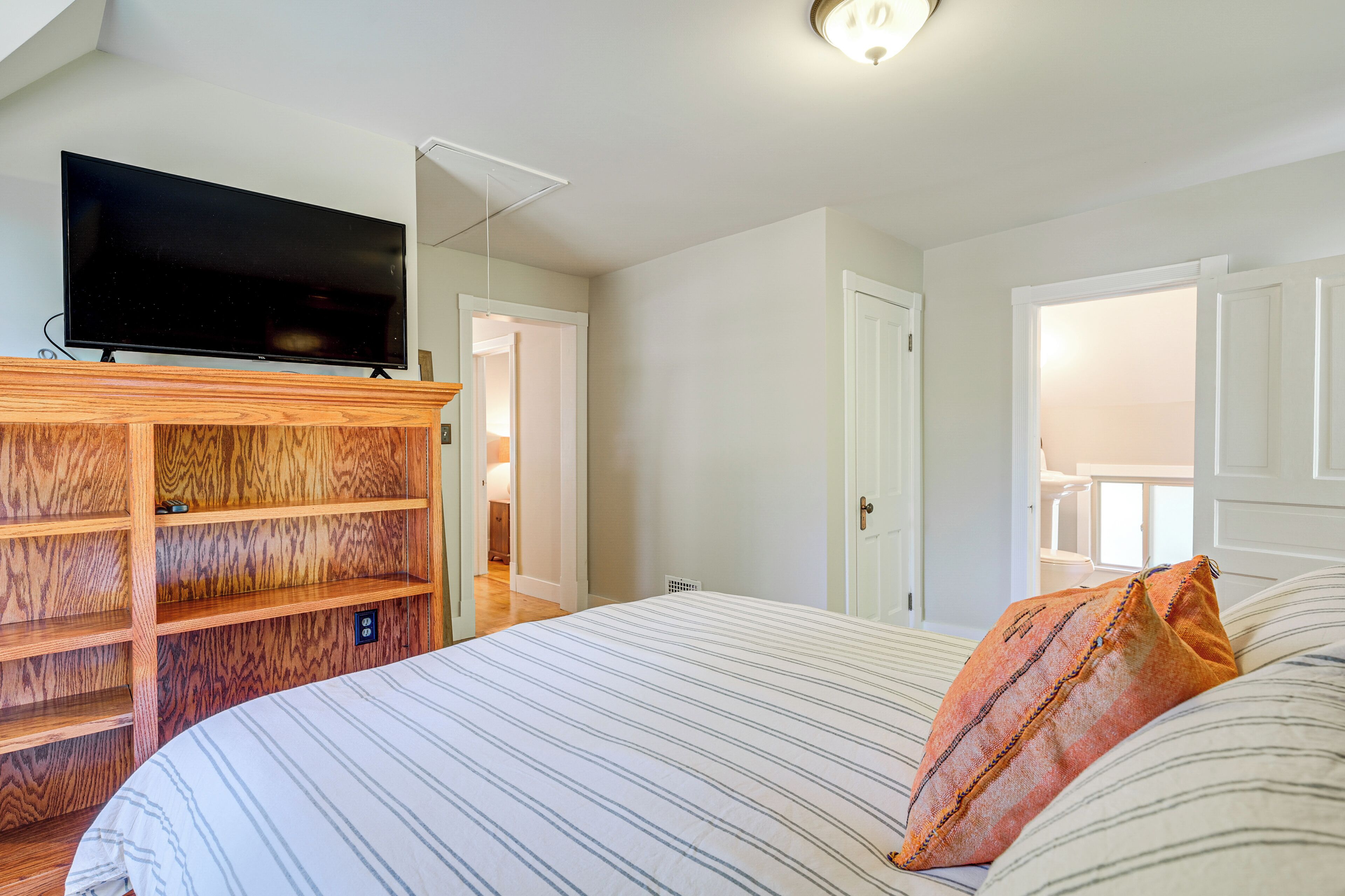 A bedroom with a bed, a television on a wooden shelf, and a door leading to another room.