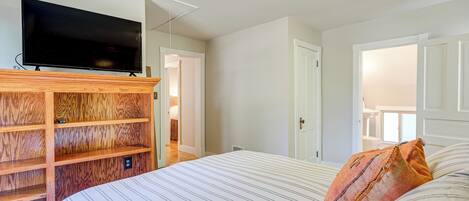 A bedroom with a bed, a television on a wooden shelf, and a door leading to another room.