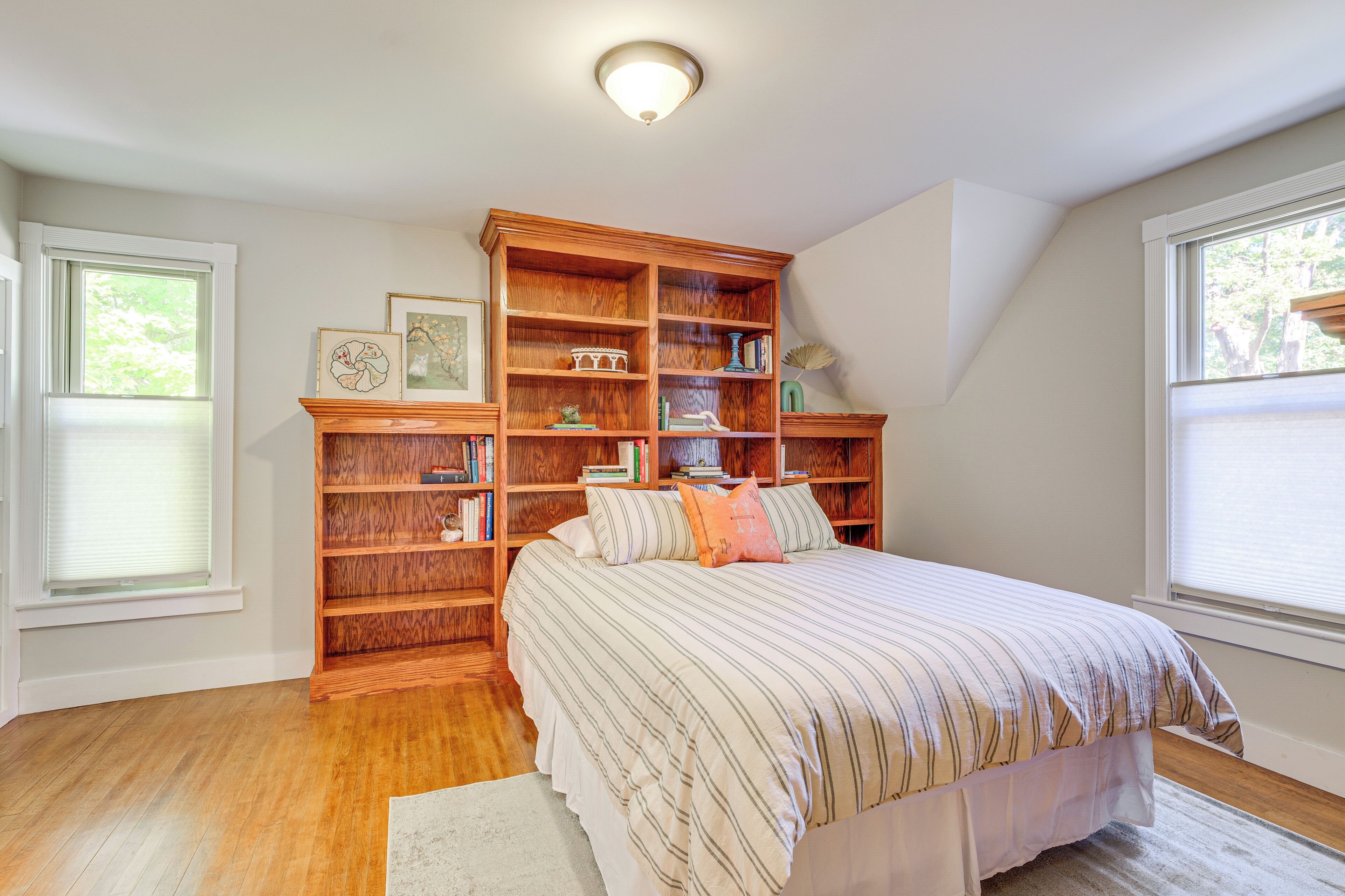 A bedroom with a large wooden bookshelf, a bed with striped bedding, and a white rug.