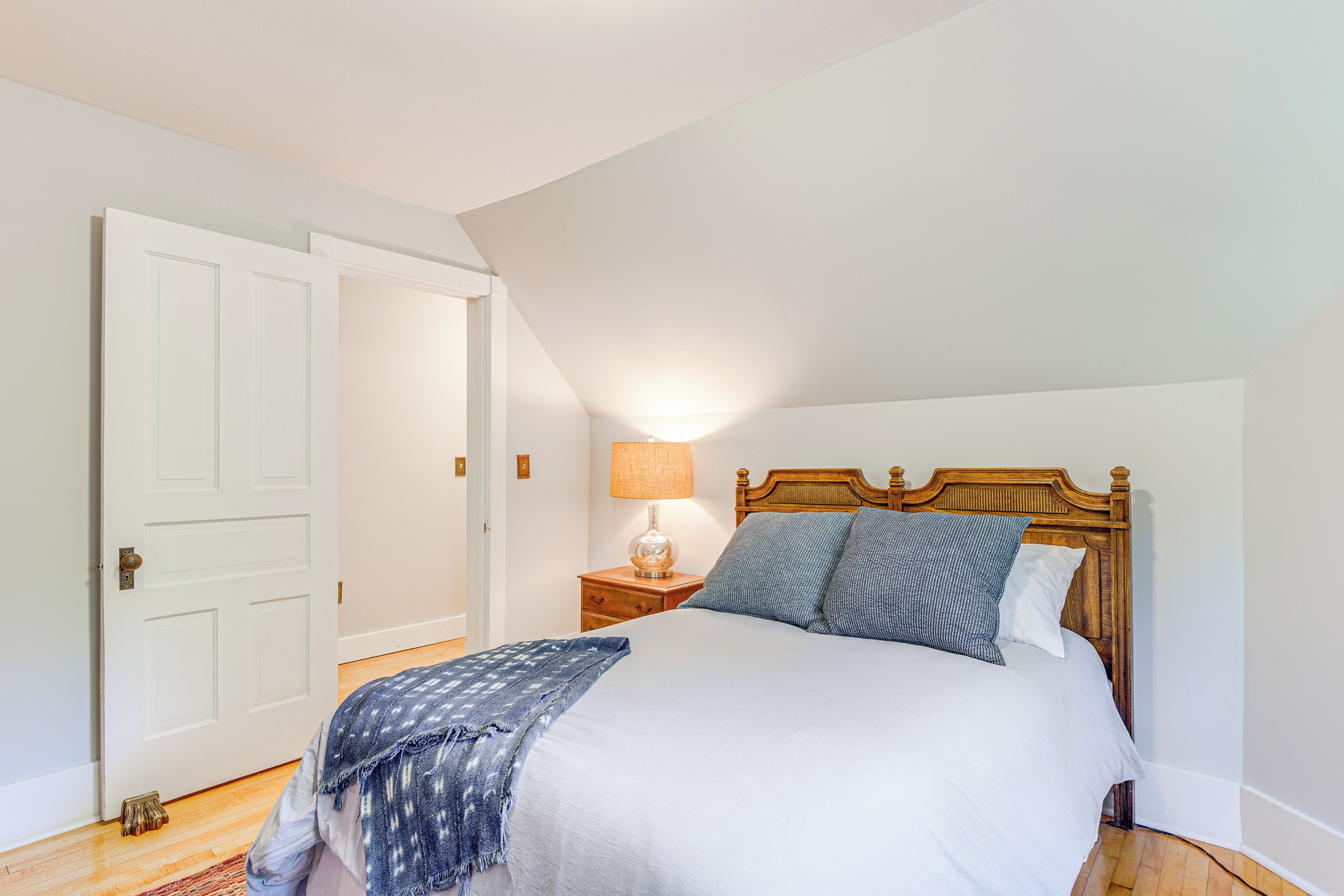 Un dormitorio con una cama, una mesita de noche, una lámpara y una puerta.