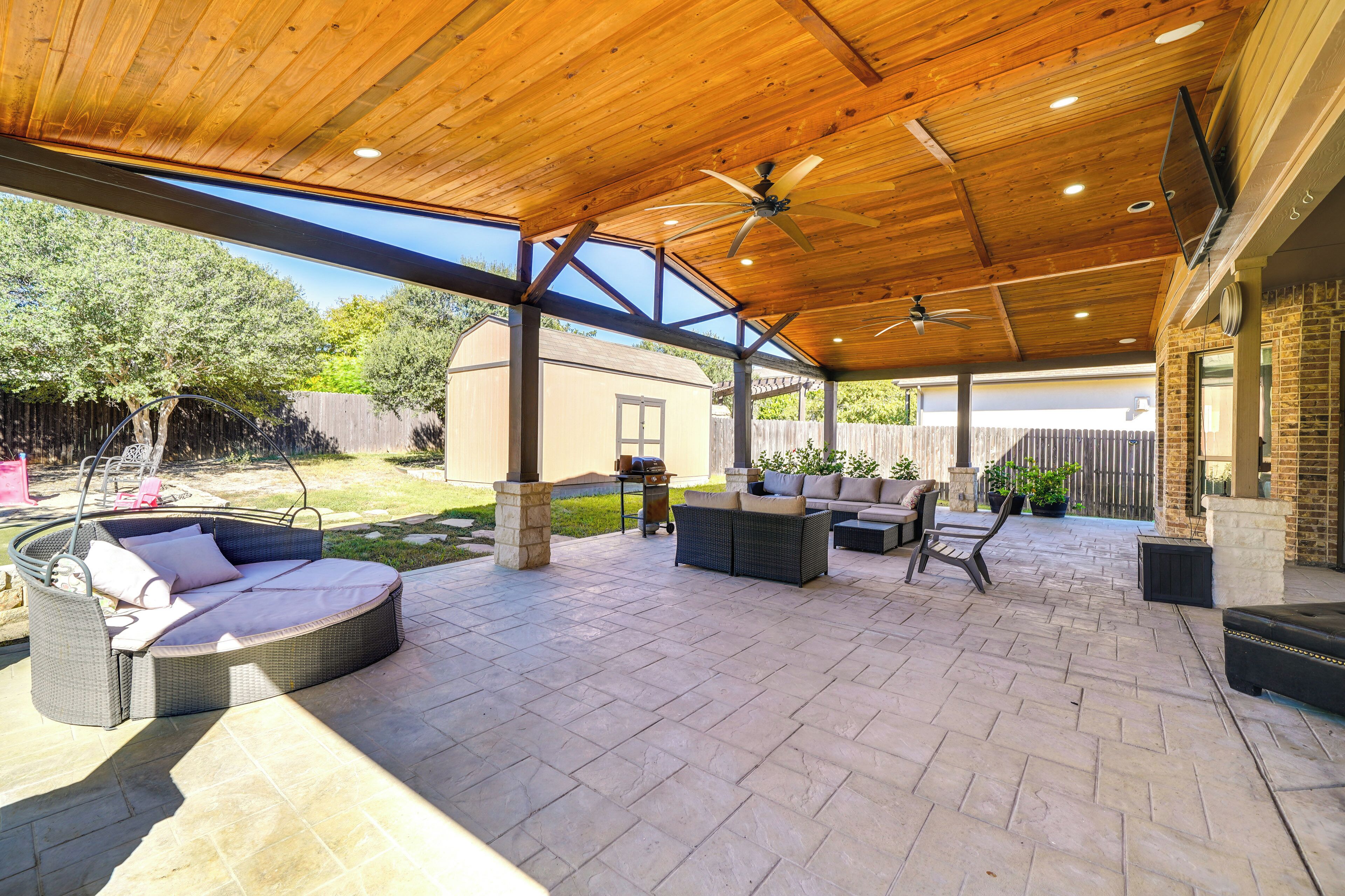 Un patio al aire libre con techo de madera, ventiladores de techo y mobiliario exterior, incluyendo un sofá y sillas.