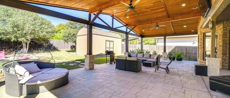 Un patio al aire libre con techo de madera, ventiladores de techo y mobiliario exterior, incluyendo un sofá y sillas.