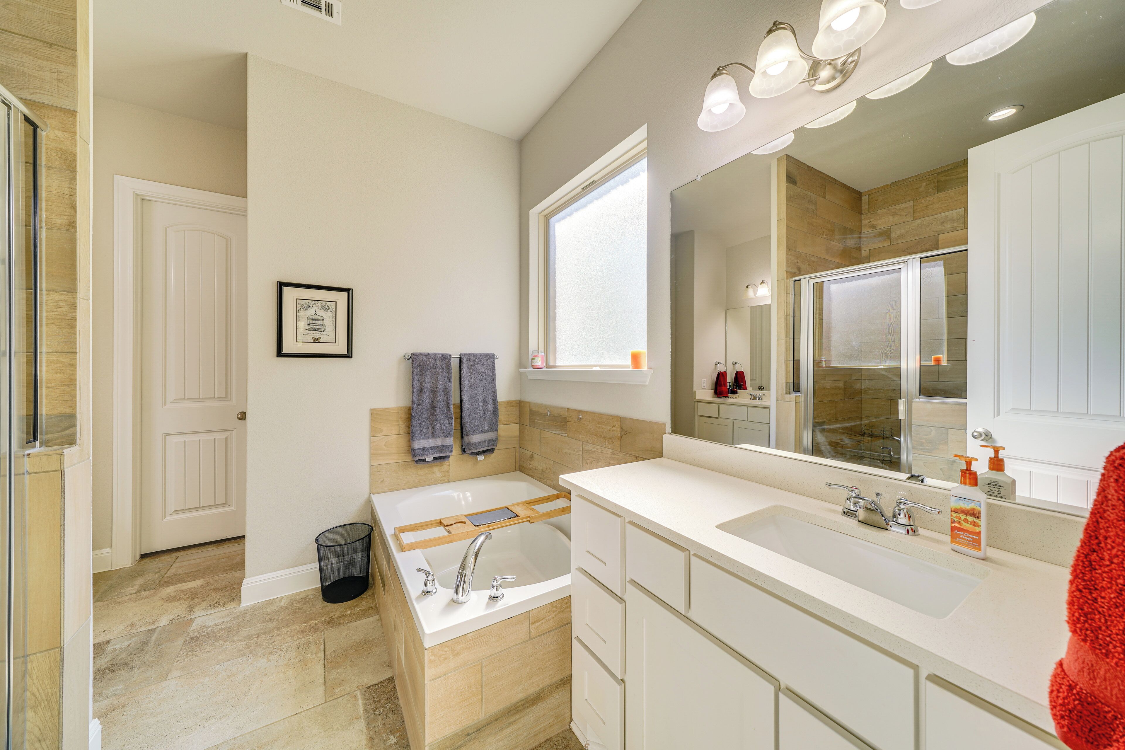 Un baño moderno con bañera, un espejo grande y un tocador con lavamanos.