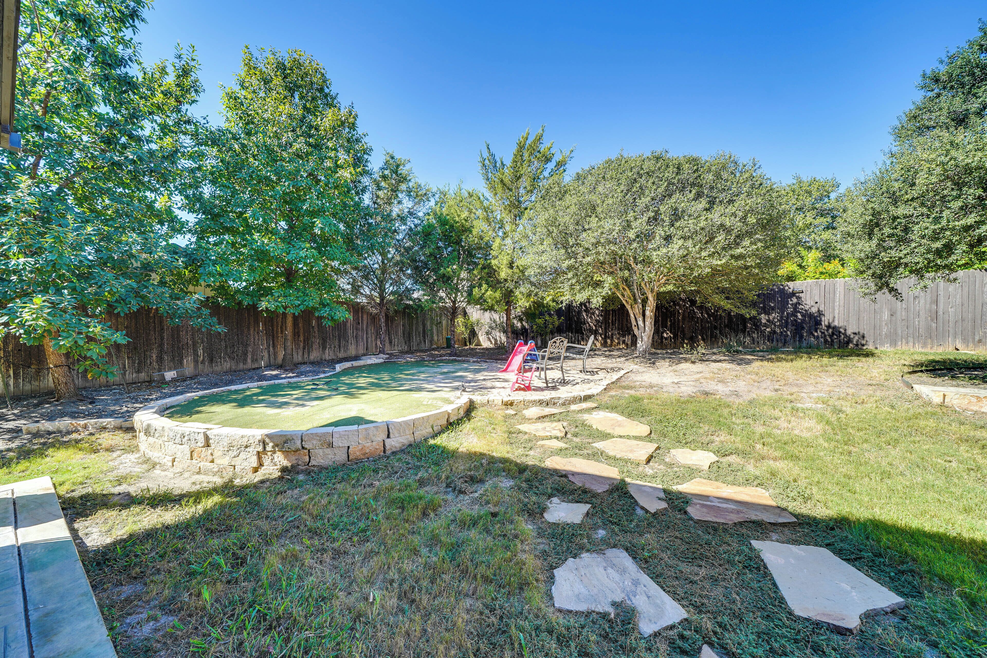 A backyard with a swimming pool, stone pathway, and wooden fence.