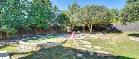 A backyard with a swimming pool, stone pathway, and wooden fence.