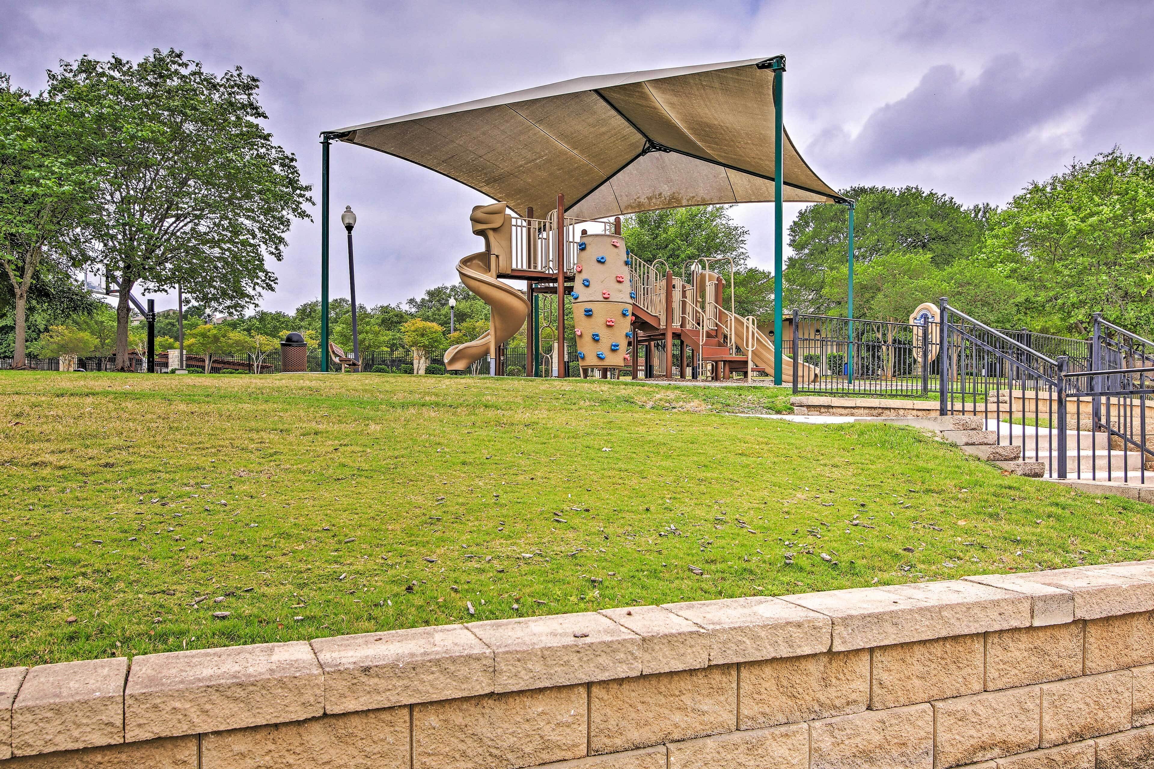 A playground with a climbing wall and slides, surrounded by a grassy area and a stone wall.