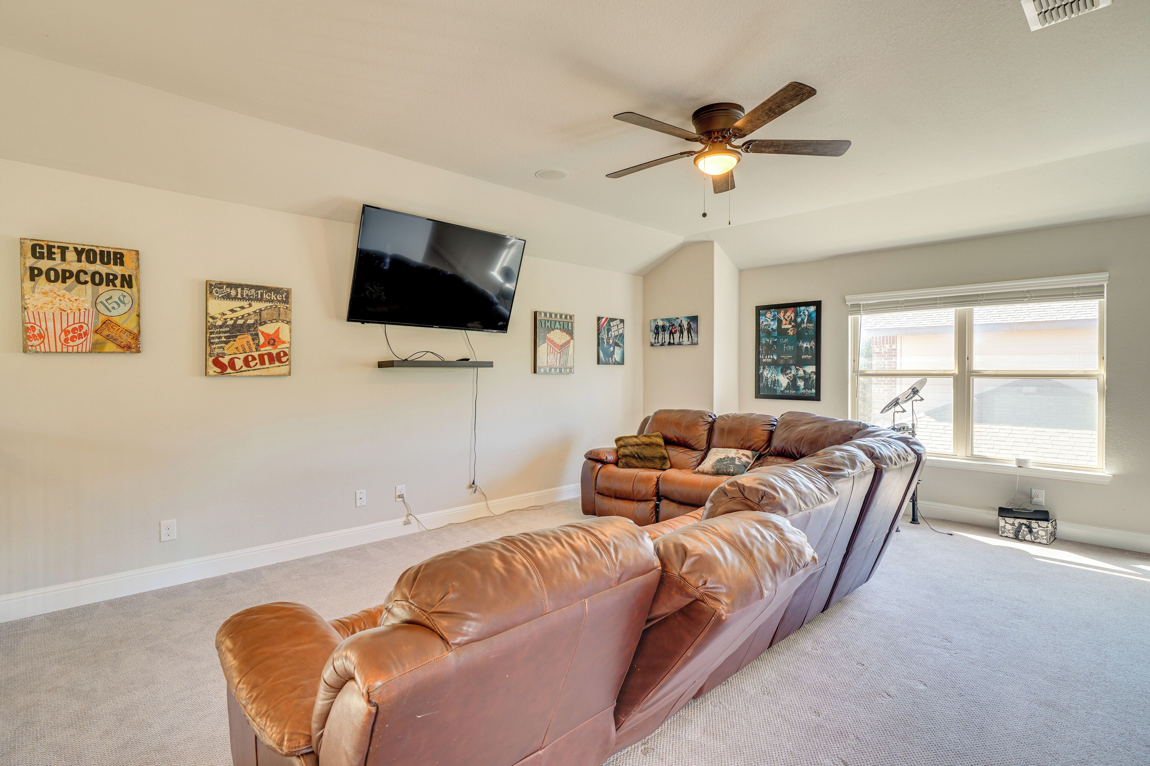 A living room with a large sectional sofa, a ceiling fan, a flat-screen TV, and artwork on the walls.