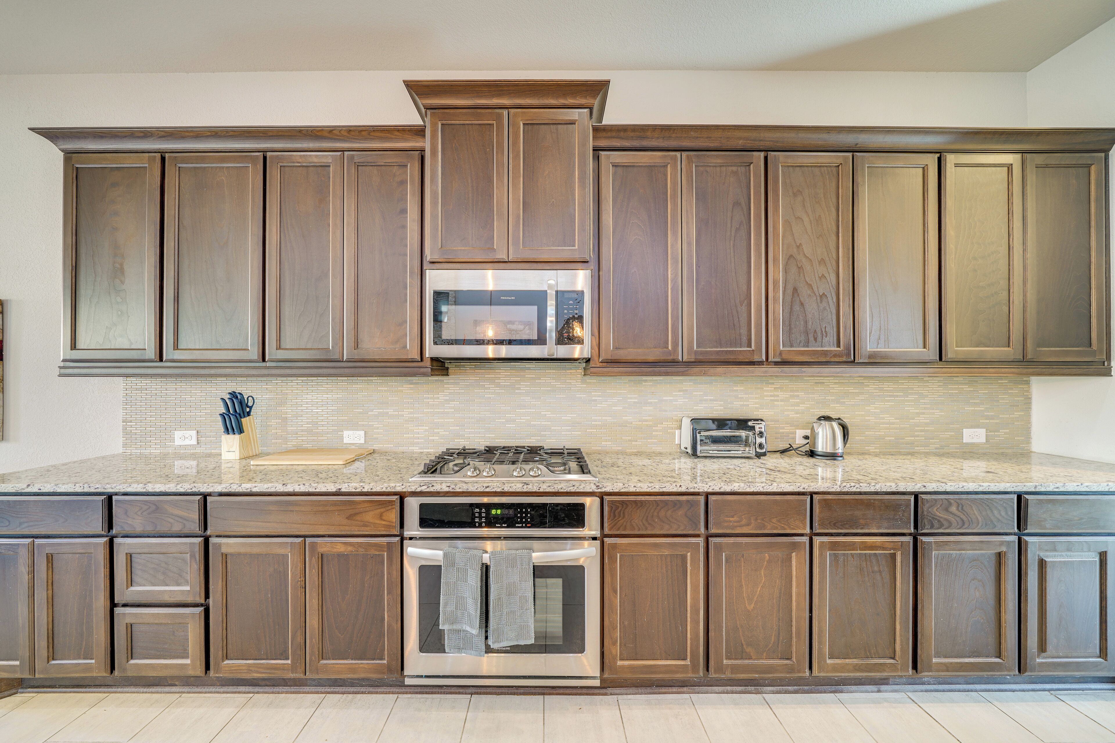 A kitchen with wooden cabinets, a stainless steel microwave, a gas stove, a built-in oven, and a granite countertop.